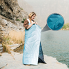 Frau und Kind in einer blauen Decke eingewickelt, stehen am Seeufer neben Felsen