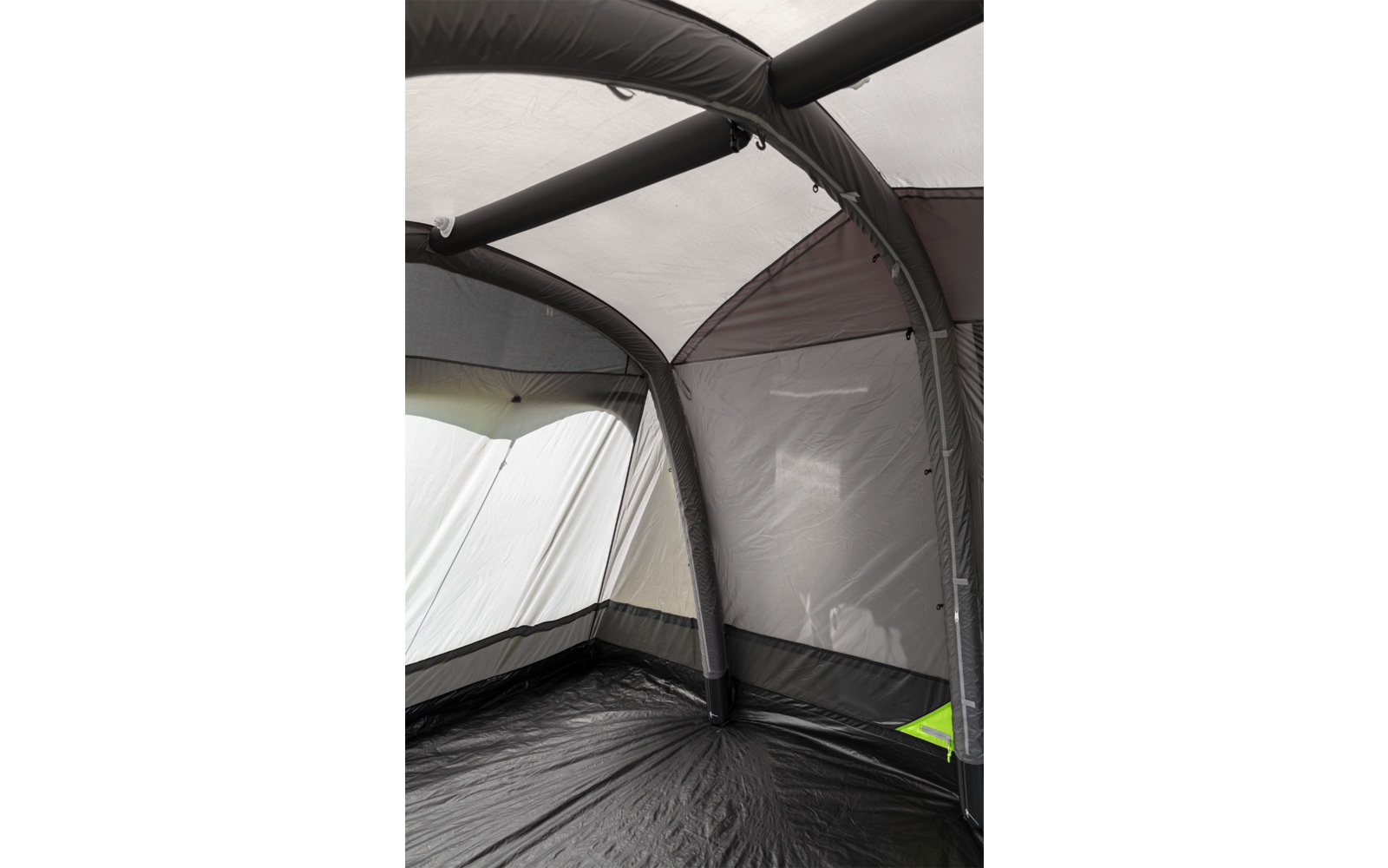 Interieur van een tent met zwarte opblaasbare bogen, grijze stofwanden, een halfdoorzichtig dak en een zwarte vloer; zichtbare naden en een groen label in een hoek