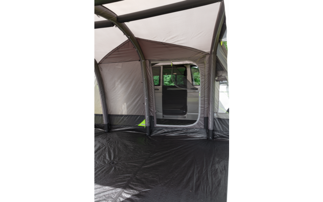 Interieur van een opblaasbare tent met zwarte vloer en lichtgrijze en bruine wanden, zicht door de opening op de geopende schuifdeur en het zijraam van een witte bestelwagen op de achtergrond