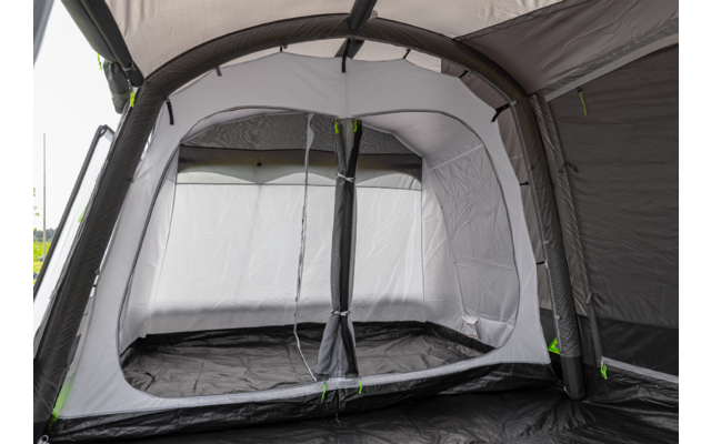 Binnenkant van een grijze tent met lichtgrijze binnenwanden, zwart grondzeil, grote rechthoekige opening met ritsen, gebogen buizen/stangen en groene ritsaccenten