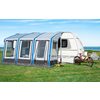 Caravane avec auvent bleu-gris attaché sur une prairie, deux vélos au premier plan, mer et ciel bleu en arrière-plan