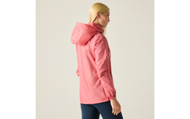 Seitliche Aufnahme einer Person mit langen blonden Haaren, die eine pinke Kapuzenjacke und dunkelblaue Leggings vor hellem Hintergrund trägt