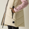 Gilet imbottito color crema con zip nera, mano destra in tasca con zip, manica in maglia rosa con motivo a spina di pesce, parte inferiore mostra leggings neri