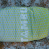 Yellow-green sleeping bag with light-green polka dots and vertical white lettering on snowy, partly grassy ground