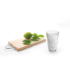 Holzbrett mit zwei grünen Limetten und einigen Minzblättern daneben ist ein leeres Glas
