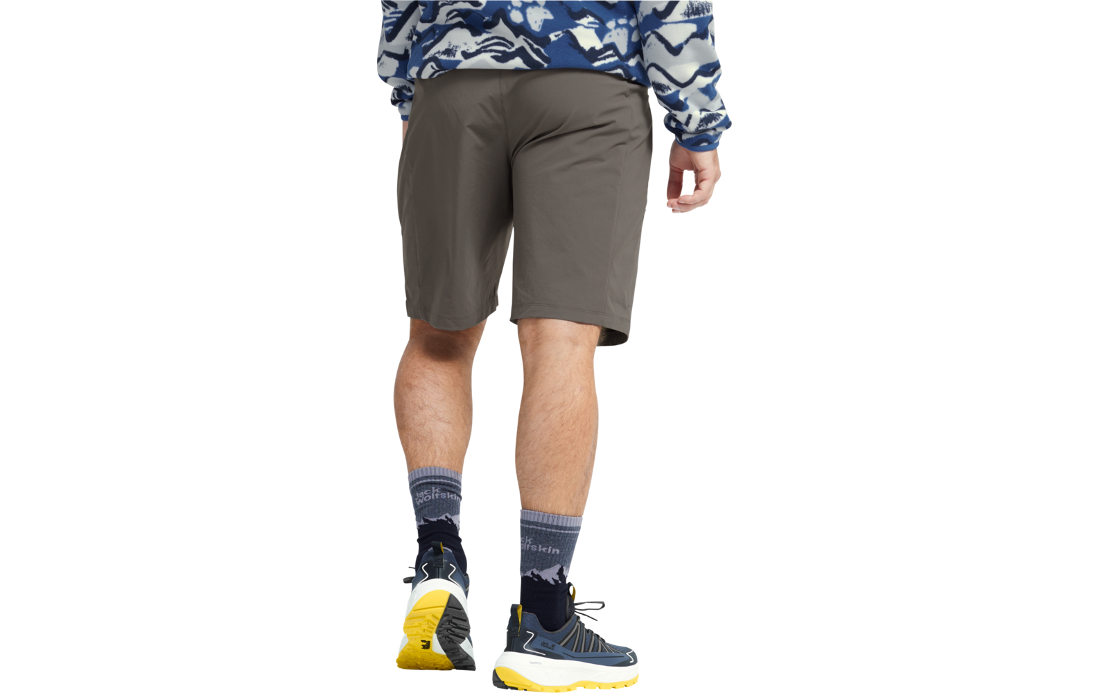 Achteraanzicht van een persoon vanaf de taille, grijze korte broek, blauw-wit dessin trui, zichtbare benen met kuitbeharing, donkere sokken met bergmotief, blauwe sportschoenen met gele zolen