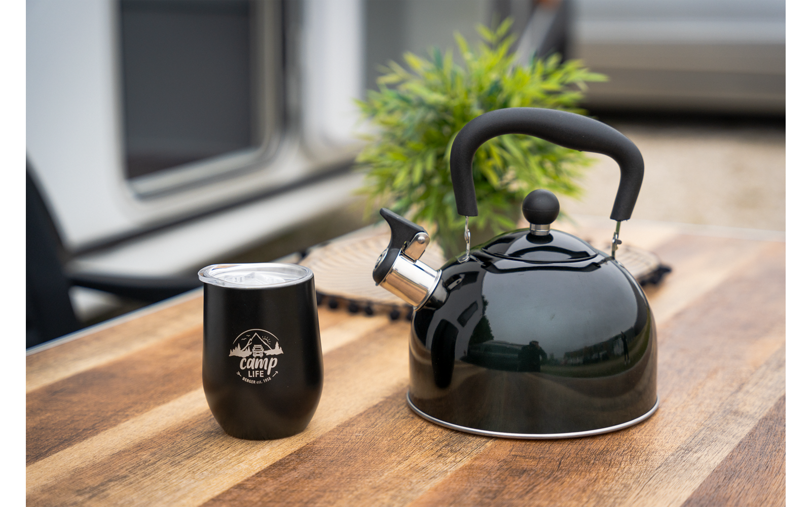 Groene waterkoker en zwarte mok op een houten tafel, plant en raam op de achtergrond