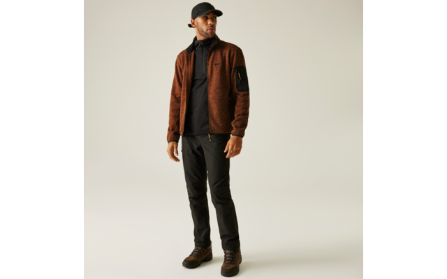 Ein Mann trägt eine braune Jacke, schwarze Hose und braune Schuhe, dazu eine schwarze Kappe