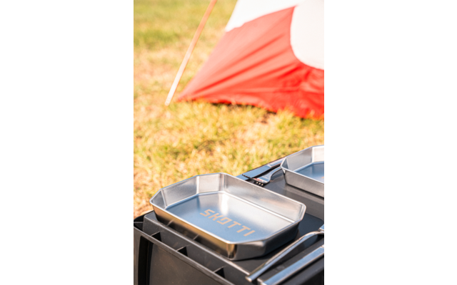 Metal pan with 'SKOTTI' lettering on a black tray, grass and a red-and-white tent in the background
