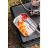 Croissant on a metal tray, knife with red jam, jar of jam at the edge, metal appliance and black plastic crate on grass