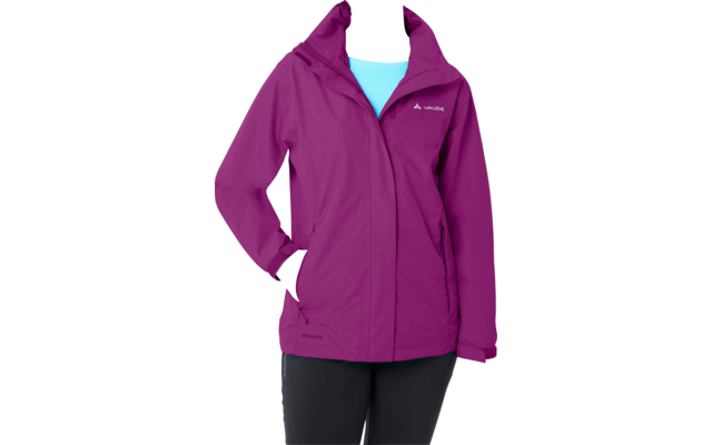 Person steht vor weißem Hintergrund, trägt violette Jacke, hellblaues Oberteil und schwarze Hose, Hände in Jackentaschen, Haare zurückgebunden