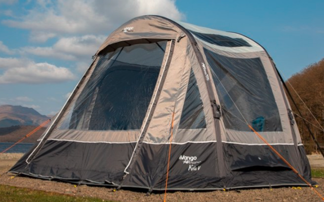 Großes graues Zelt steht auf grünem Gras mit Bergen und blauem Himmel im Hintergrund