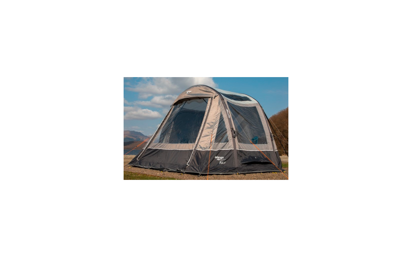 Großes graues Zelt steht auf grünem Gras mit Bergen und blauem Himmel im Hintergrund