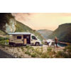 Camper van parked by a riverbank with mountains in the background, man casting fishing line