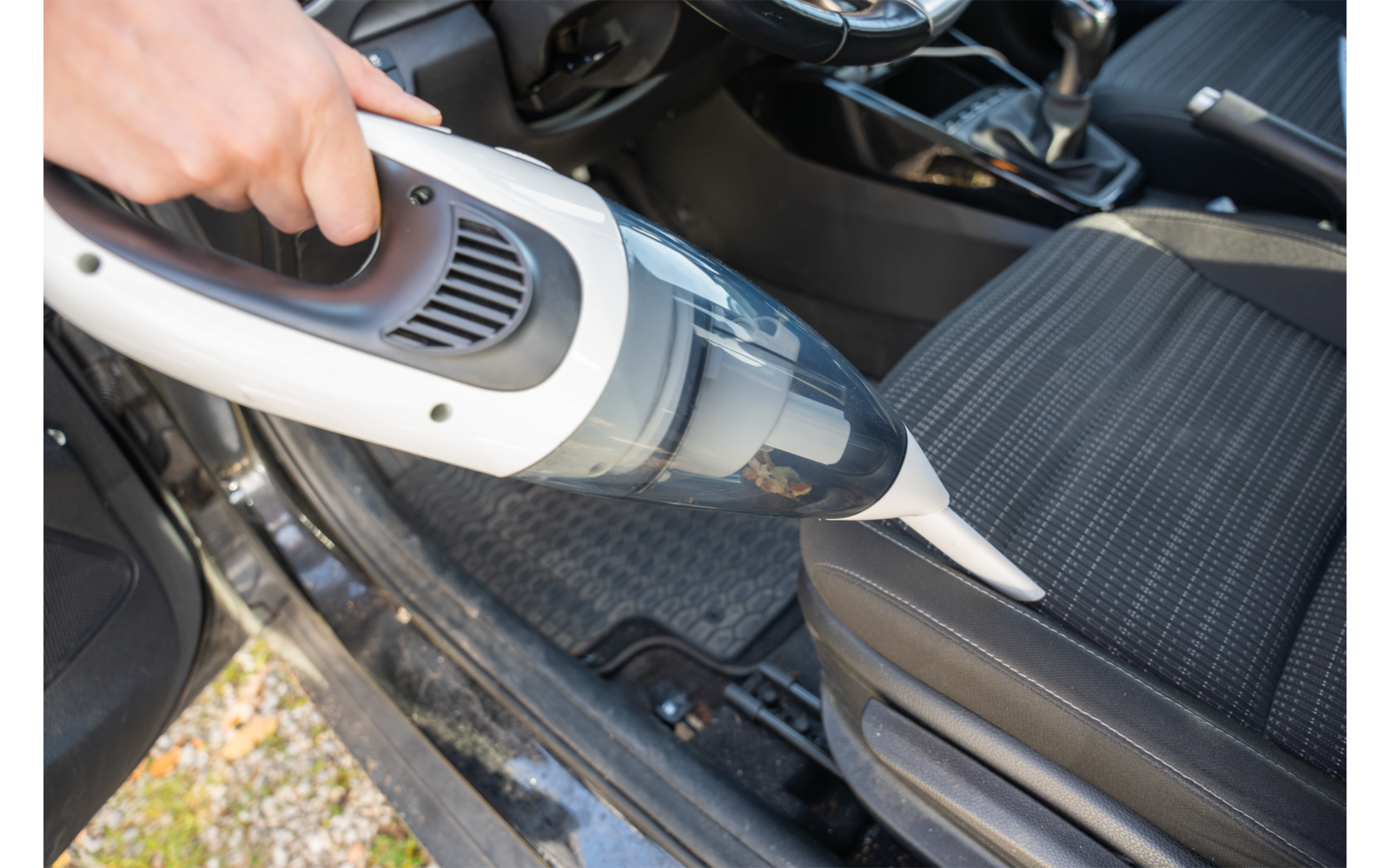 Main tenant un aspirateur à main sans fil avec suceur d'angle sur un siège de voiture