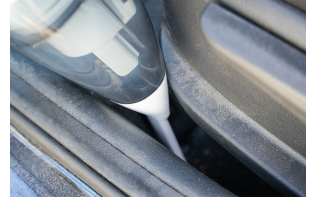 Embout d'aspirateur blanc et gris inséré dans une étroite fente poussiéreuse entre deux surfaces plastiques gris foncé
