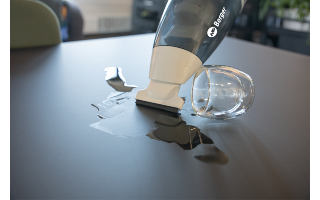 Aspirateur à main aspire du liquide sur une table sombre à côté d'un verre renversé