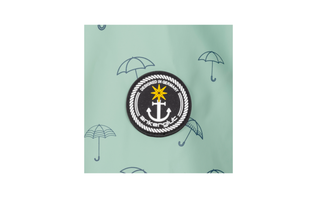 Ronde zwarte patch met witte anker, gele ster erboven, witte touwrand en tekst 'DESIGNED IN GERMANY' en 'ankerglück' op een mintgroene achtergrond met kleine paraplu-illustraties