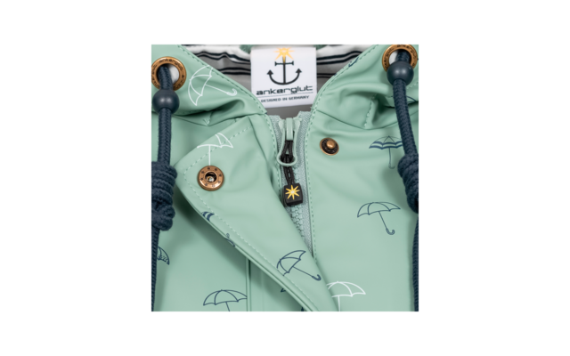 Close-up van de kraag van een mintgroene jas met rits, metalen drukknopen, donkere koorden, paraplupatroon en een stoffen label met een anker