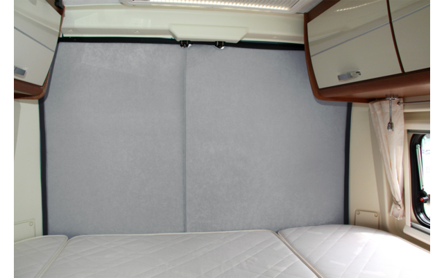 Blick auf ein geschlossenes graues Vorhangpaneel in einem Wohnmobil mit sichtbaren Betten und Schränken