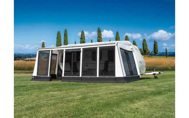 Weißes Wohnwagen-Vorzelt auf grünem Gras mit Bäumen und blauem Himmel im Hintergrund