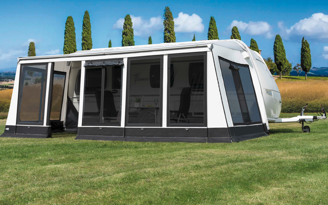 Witte caravanluifel op groen gras met bomen en blauwe lucht op de achtergrond