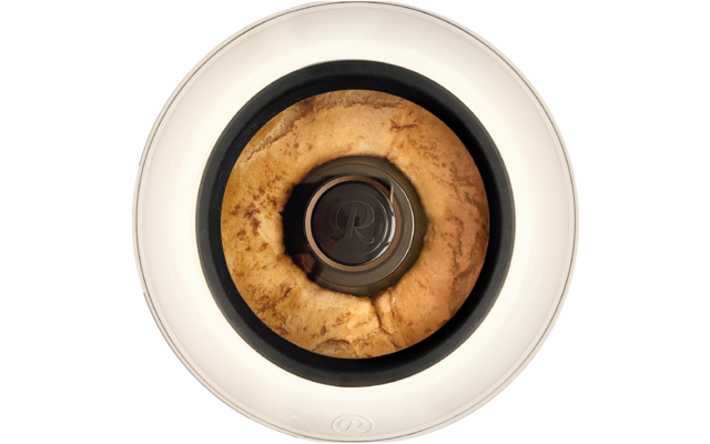 Draufsicht auf ein goldbraunes, ringförmiges Gebäck in einem weißen runden Behälter mit schwarzem Rand und zentralem Metallknopf mit eingeprägtem ‚R‘