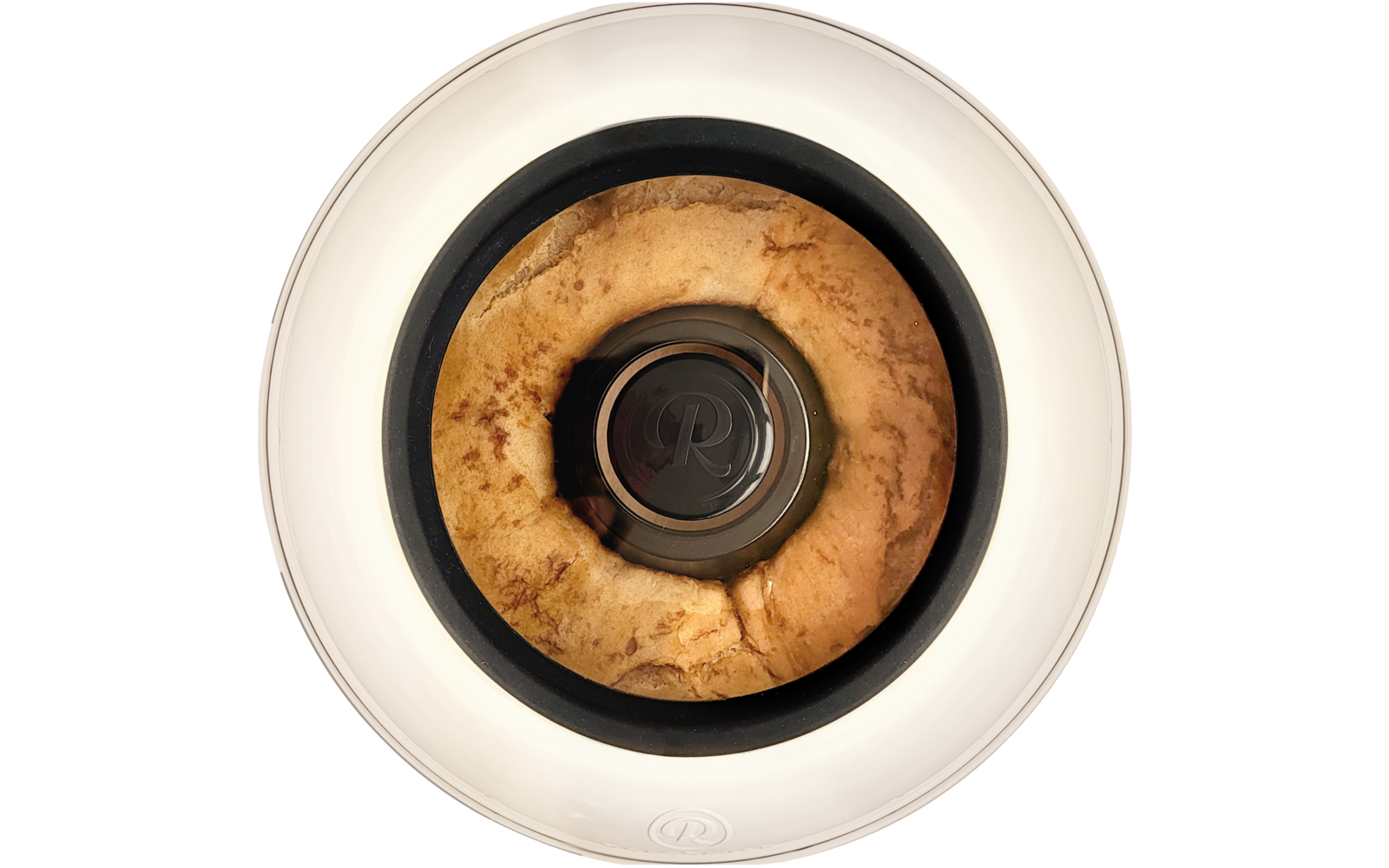Draufsicht auf ein goldbraunes, ringförmiges Gebäck in einem weißen runden Behälter mit schwarzem Rand und zentralem Metallknopf mit eingeprägtem ‚R‘