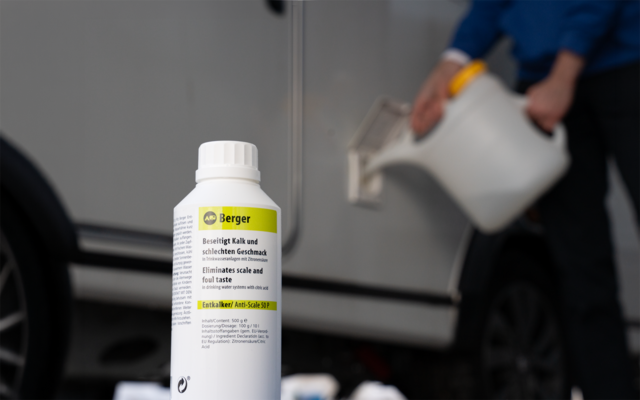 Weiße Kunststoffflasche mit 'Berger'-Etikett im Vordergrund; im Hintergrund gießt eine Person aus einem weißen Kanister in eine offene Seitenöffnung eines Fahrzeugs