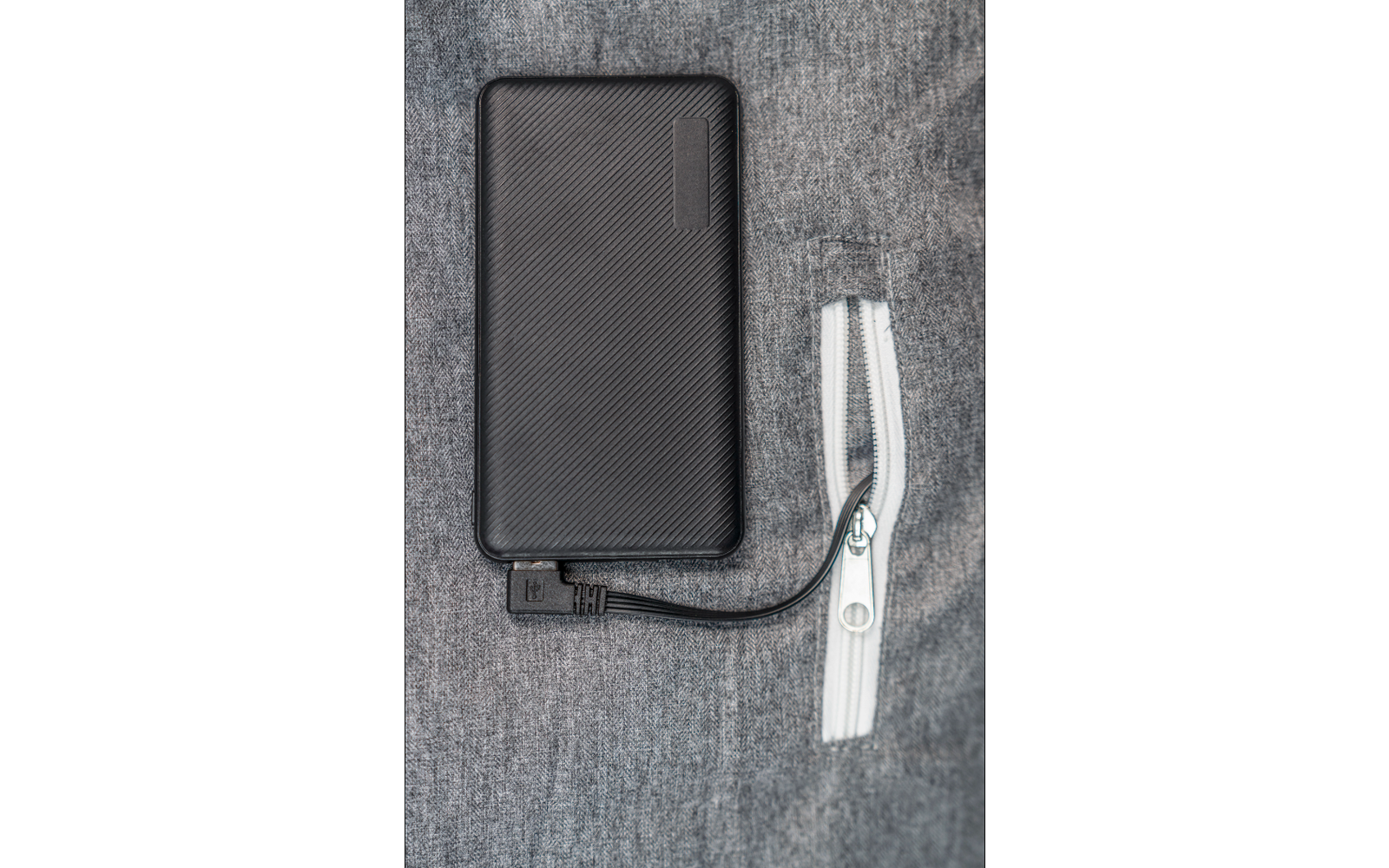 Schwarze Powerbank mit angeschlossenem weißen Ladekabel auf grauem Stoffhintergrund