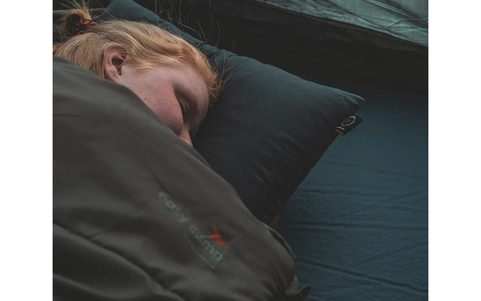Person liegt schlafend auf einem schwarzen Kissen und einer dunklen Unterlage