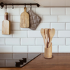 Kitchen countertop with cooktop, wooden utensils in a holder; two wooden cutting boards and a gray oven mitt hanging on a rail in front of white tiled backsplash