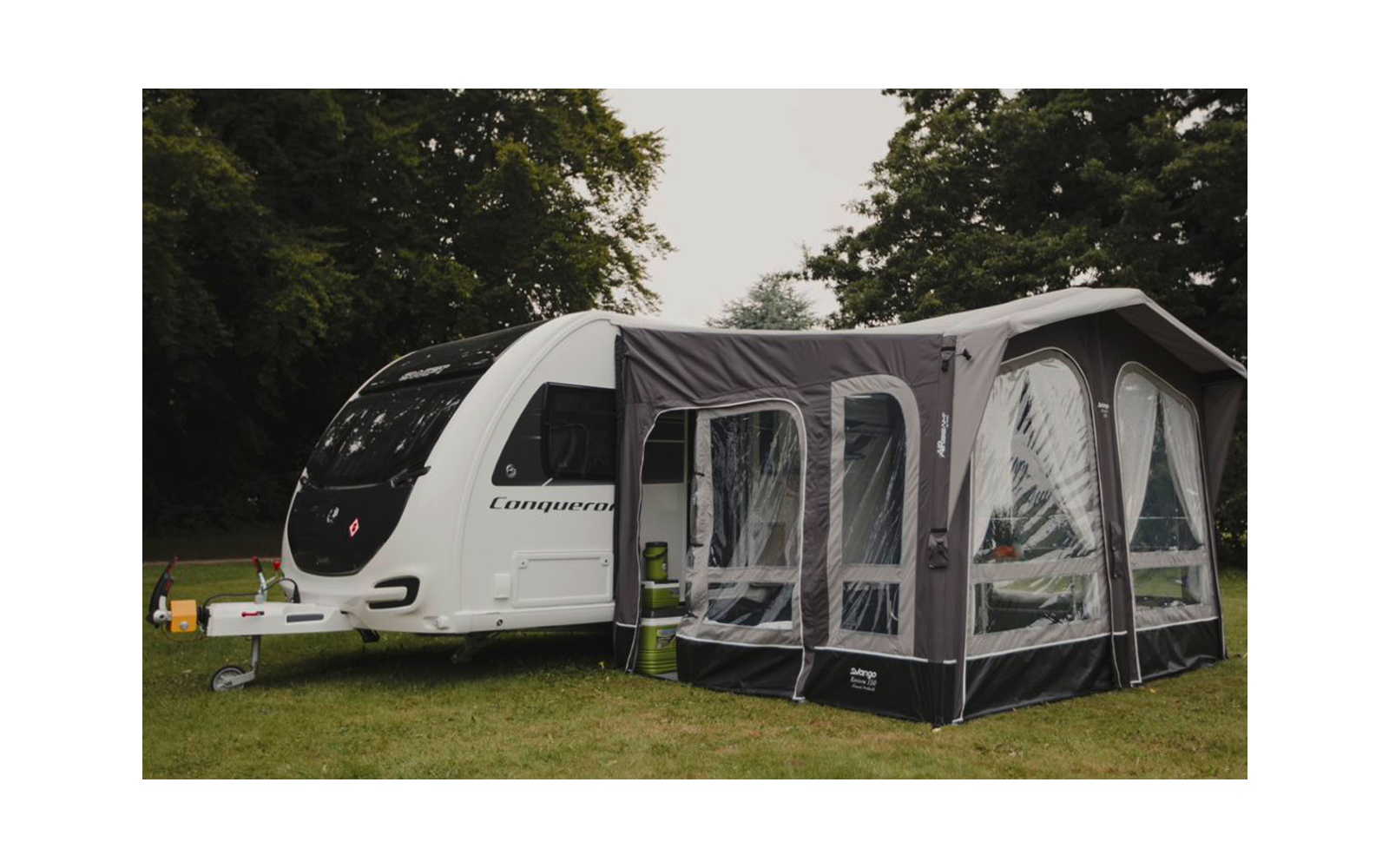 Wohnwagen mit angebautem Vorzelt auf einer grünen Wiese, umgeben von Bäumen