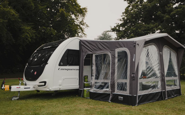 Wohnwagen mit angebautem Vorzelt auf einer grünen Wiese, umgeben von Bäumen