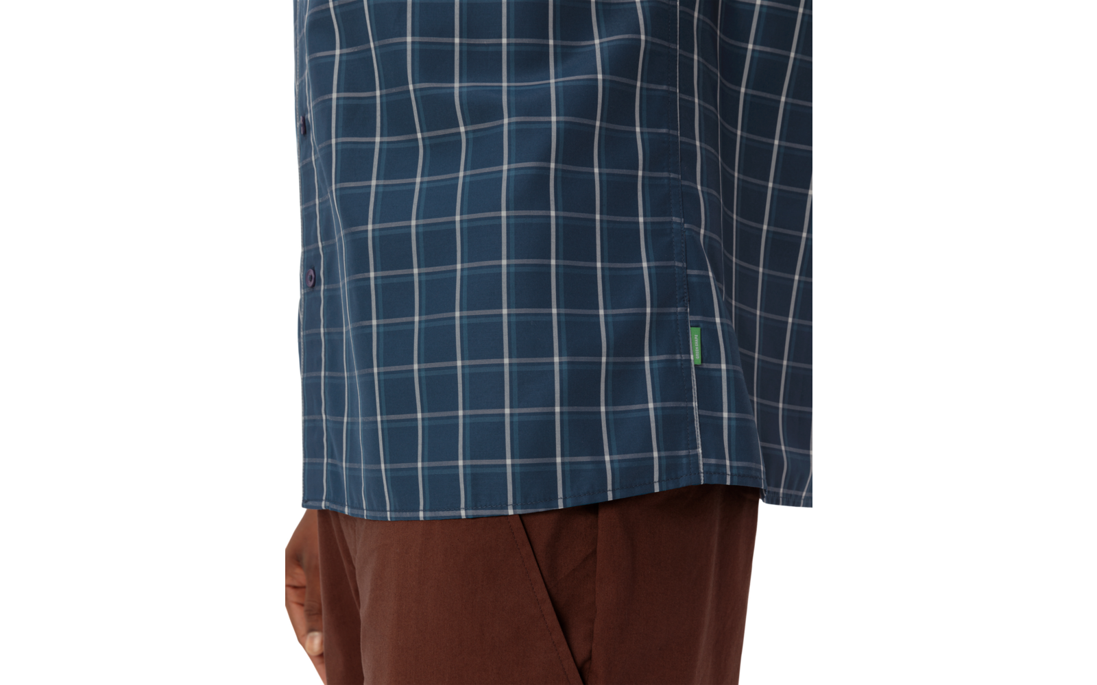 Unterer Bereich eines blau-karierten Hemds mit kleinem grünem Seitenschild über brauner Hose, Hand am Bildrand