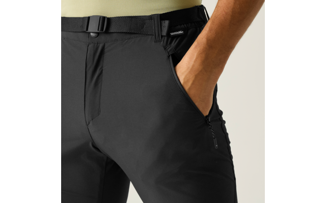 Nahaufnahme des Hüftbereichs einer Person mit schwarzer Hose und Gurtbandgürtel, rechte Hand in Vordertasche, seitlicher Reißverschluss an der Tasche, Saum eines beigefarbenen Oberteils sichtbar