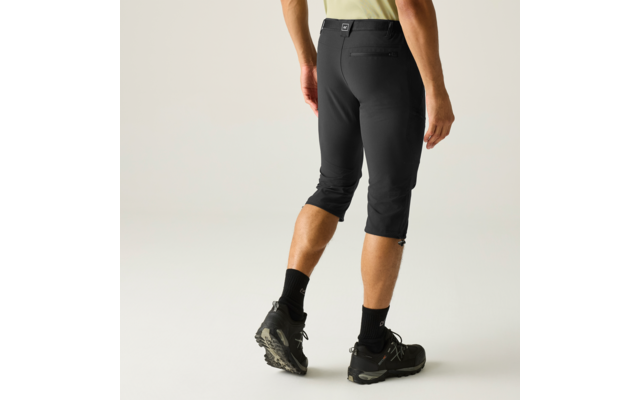 Rückansicht einer stehenden Person von Taille bis Waden, trägt dreiviertellange schwarze Hose, schwarze Socken und schwarze Wanderschuhe, heller Oberteilansatz sichtbar