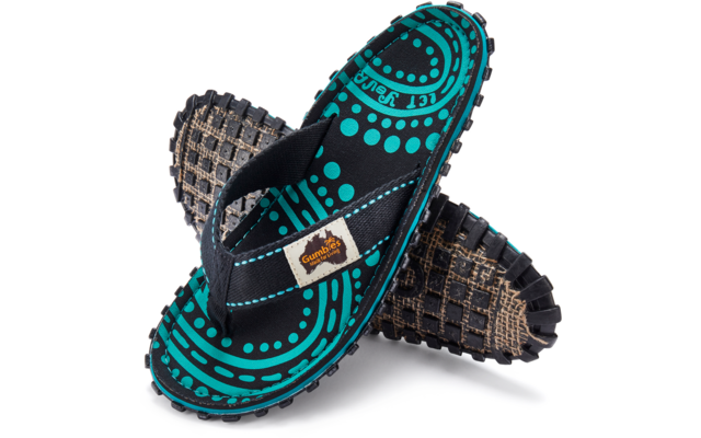 Two overlapping flip-flops with black thong strap, turquoise-and-black dot-and-circle pattern on the footbed, beige brand label on the strap, rugged sole with square tread pattern