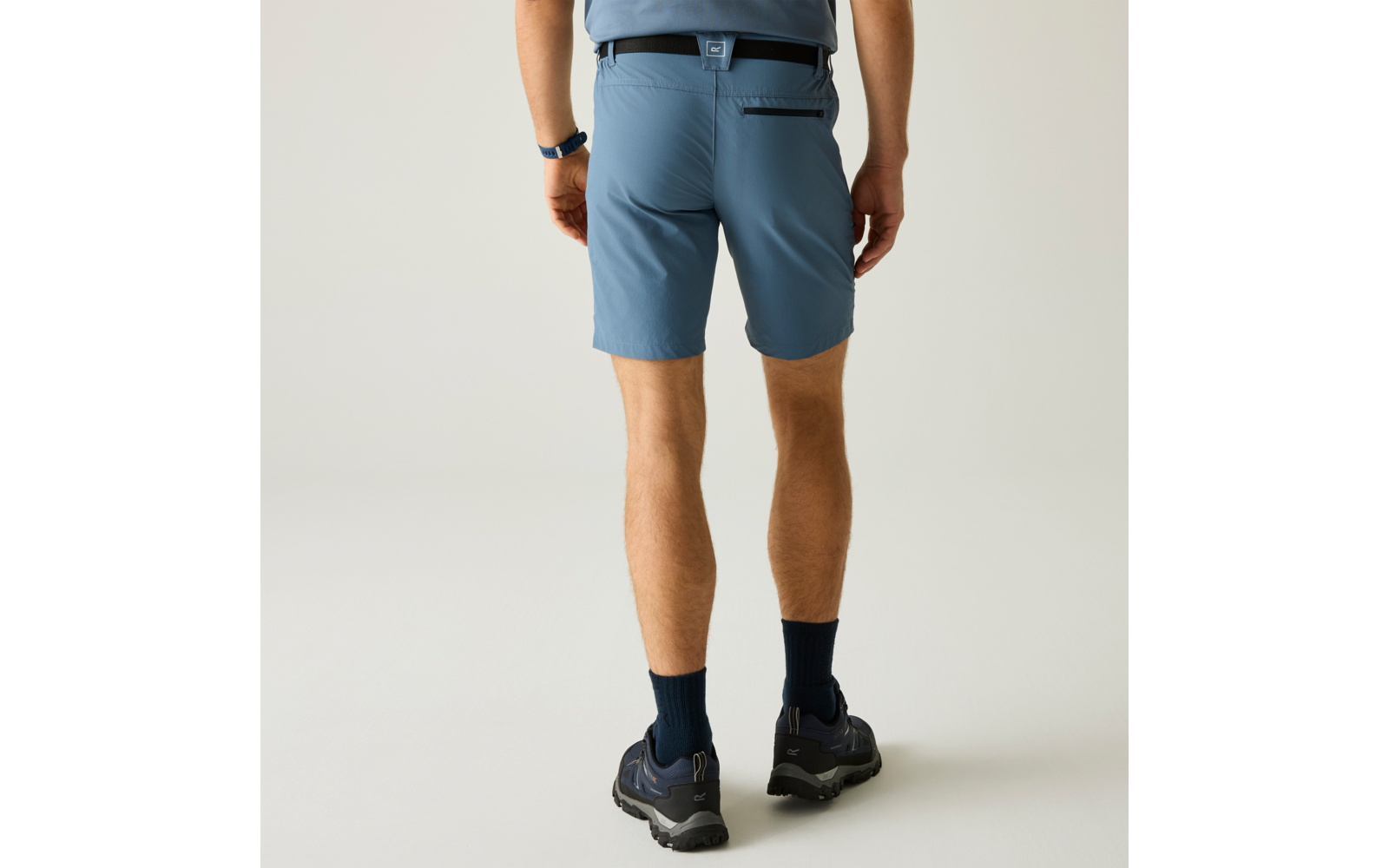 Rückenansicht einer Person von der Taille abwärts, trägt hellblaue Shorts, dunkle Kniesocken, dunkle Wanderschuhe und eine Smartwatch am linken Handgelenk