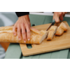 Twee handen snijden een stokbrood met een mes op een houten snijplank