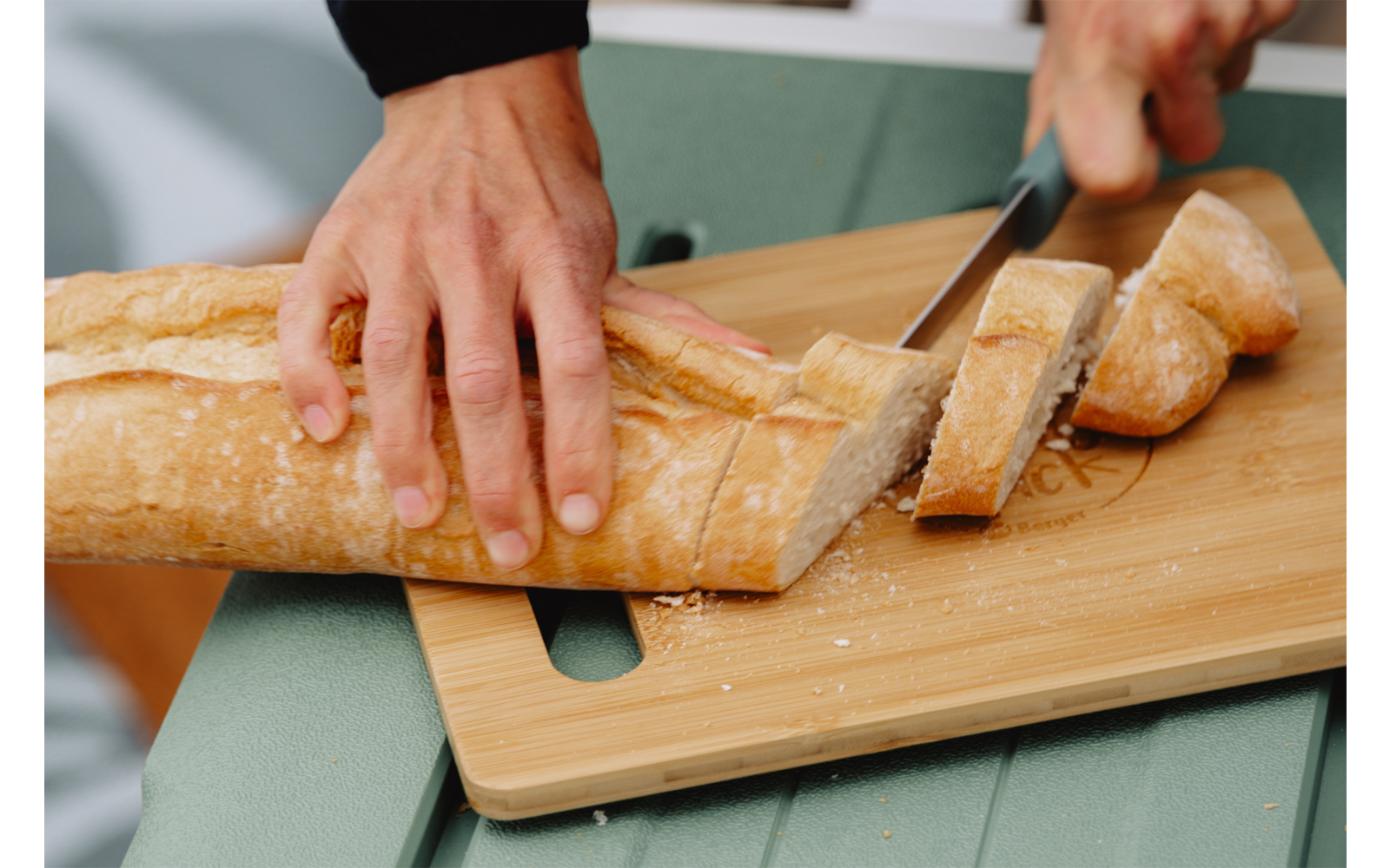 Twee handen snijden een stokbrood met een mes op een houten snijplank
