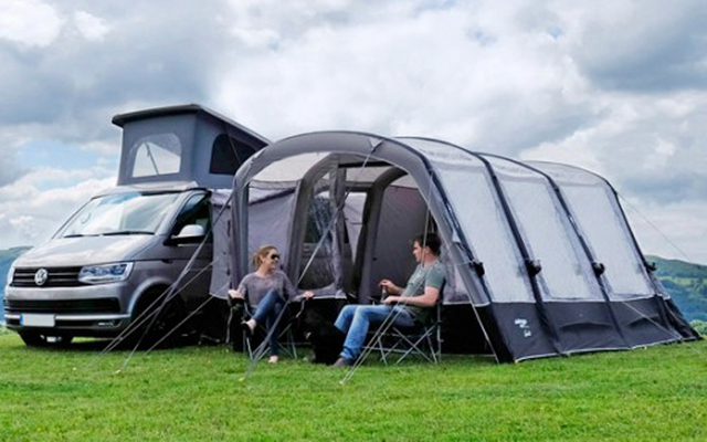 Autocaravana con tienda adjunta en un campo de césped bajo un cielo nublado