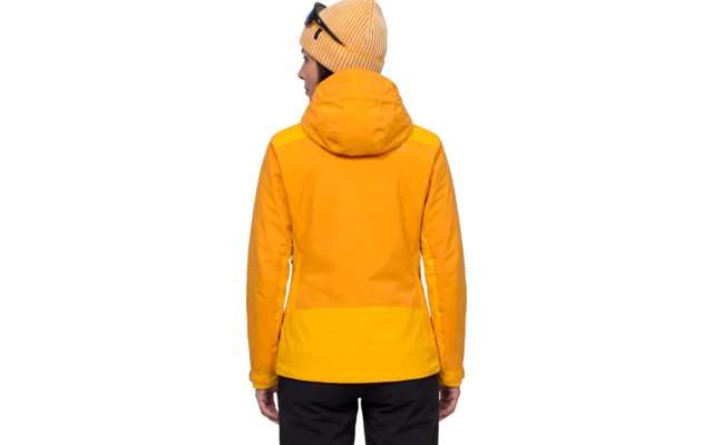 Person von hinten, trägt gelbe Strickmütze mit aufgesetzter Sonnenbrille, gelb-orange Jacke mit Kapuze und schwarze Hose