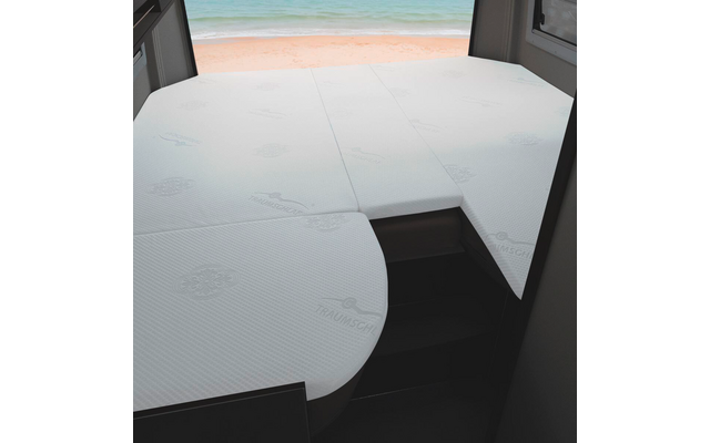 Drei weiße Matratzenstücke auf einer Bettfläche im Innenraum, Fenster mit Blick auf Sandstrand und Meer