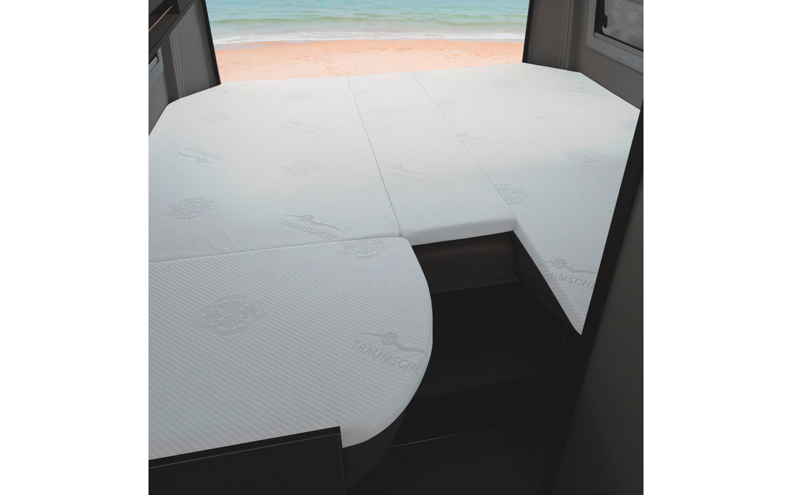 Drei weiße Matratzenstücke auf einer Bettfläche im Innenraum, Fenster mit Blick auf Sandstrand und Meer