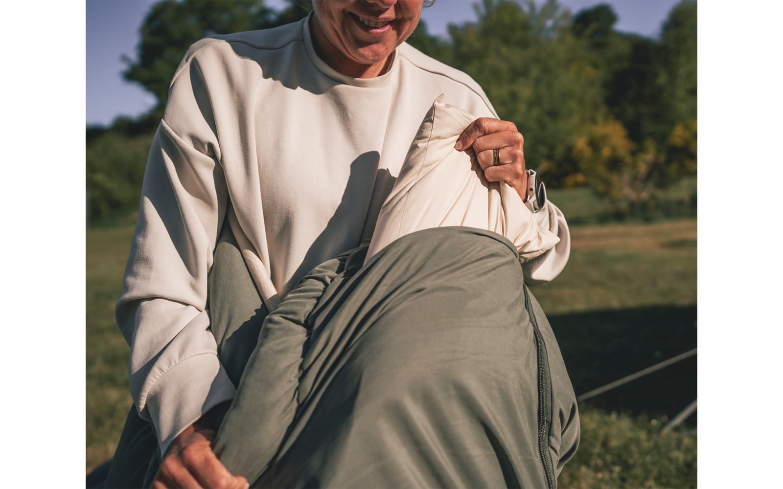 Persoon in beige trui trekt een groene jas uit, handen houden de jas vast, buiten
