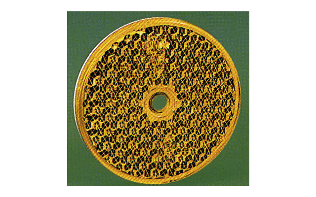 Disco redondo de color dorado con un patrón denso similar a una malla y un agujero circular en el centro sobre un fondo verde