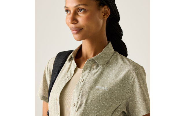 Dreiviertelansicht einer Frau mit geflochtenem Haar, die ein hellgrünes, kurzärmeliges, gemustertes Hemd über einem beigen Top trägt und einen schwarzen Rucksackriemen über der Schulter hat