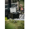 Offene schwarze tragbare Kühlbox auf Metallständer vor einem Van, daneben ein gepolsterter Campingstuhl und eine Bodenmatte auf Gras