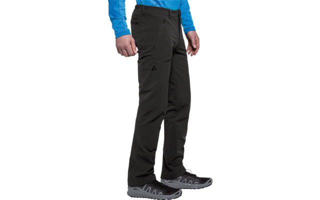 Parte inferior del cuerpo de una persona de pie con pantalones softshell negros, una prenda azul de manga larga y zapatillas de senderismo gris-negro; manos a los lados